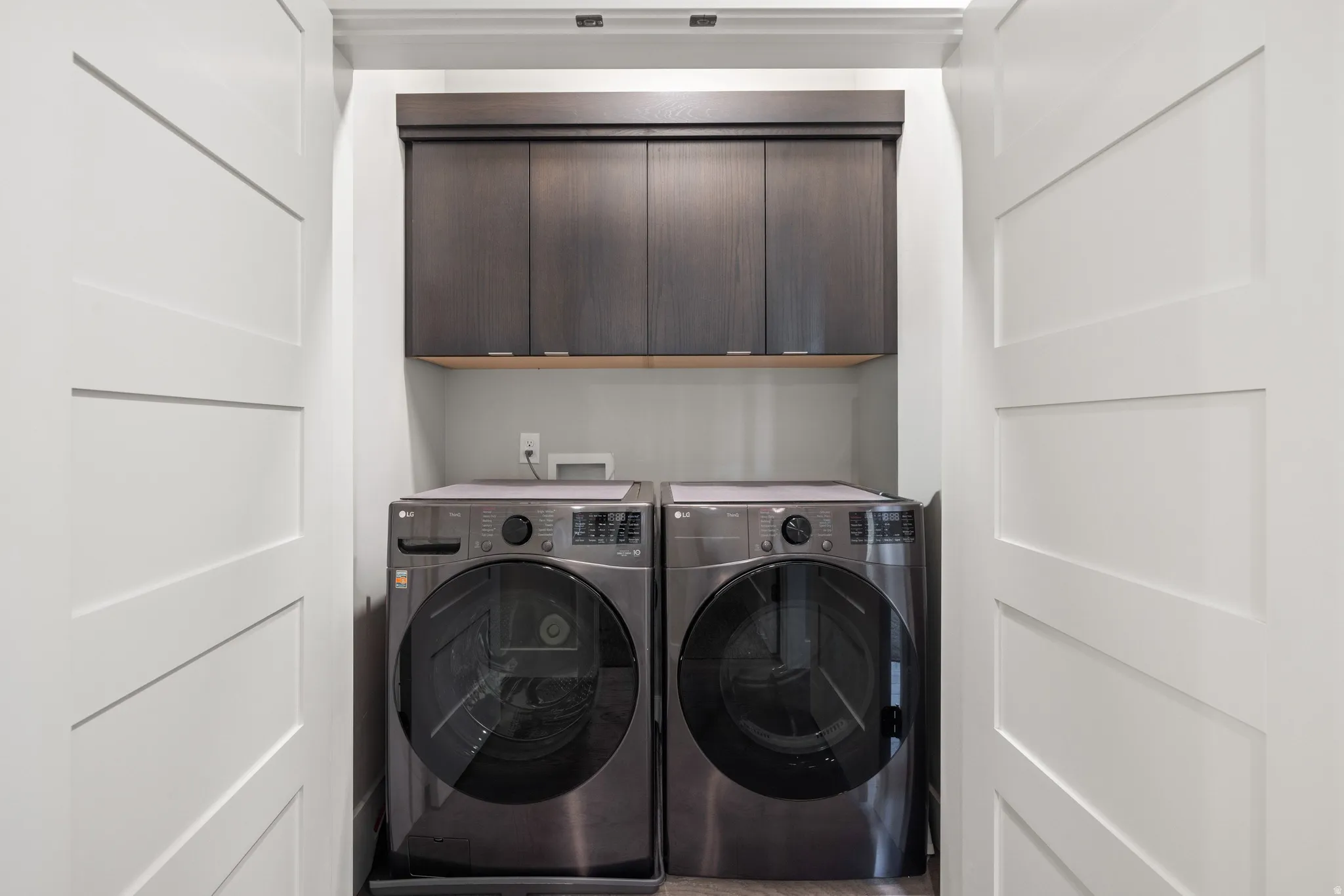 Dedicated laundry area featuring dark wood cabinetry, a light wood shelf, and a gray wall finish