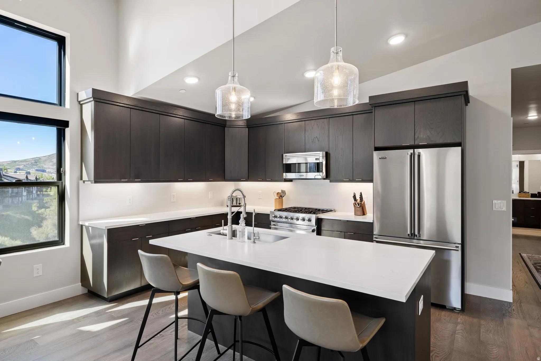 Contemporary kitchen featuring dark wood-finish cabinetry, stainless steel appliances, a center island with a white countertop, and large windows