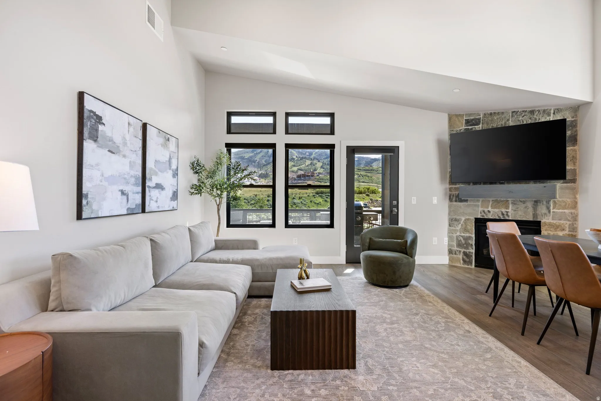 Vaulted ceilings enhance this open-concept living space, featuring wood-finish flooring and a stone-clad fireplace with a hearth