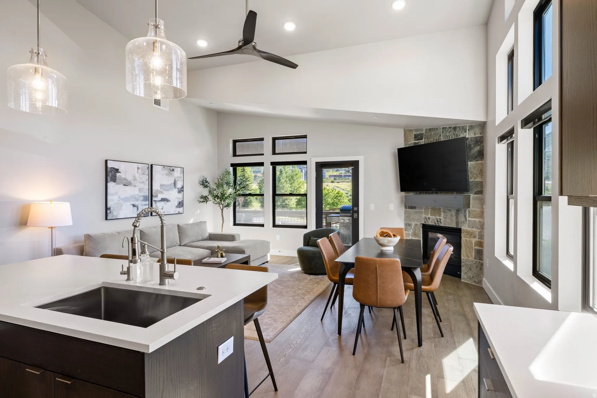 Open-concept living area with vaulted ceilings, wood-finish flooring, and a stone-clad fireplace