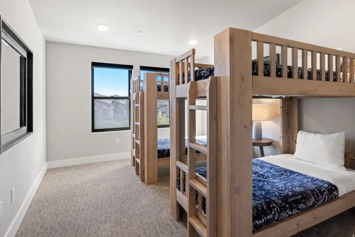Room featuring two bunk bed structures with natural wood finish, light gray carpet flooring, and white painted walls