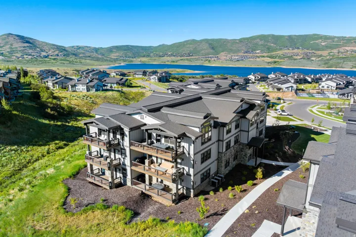 Modern multi-story building featuring stacked balconies, stone veneer accents, vertical siding, and a dark shingle roof