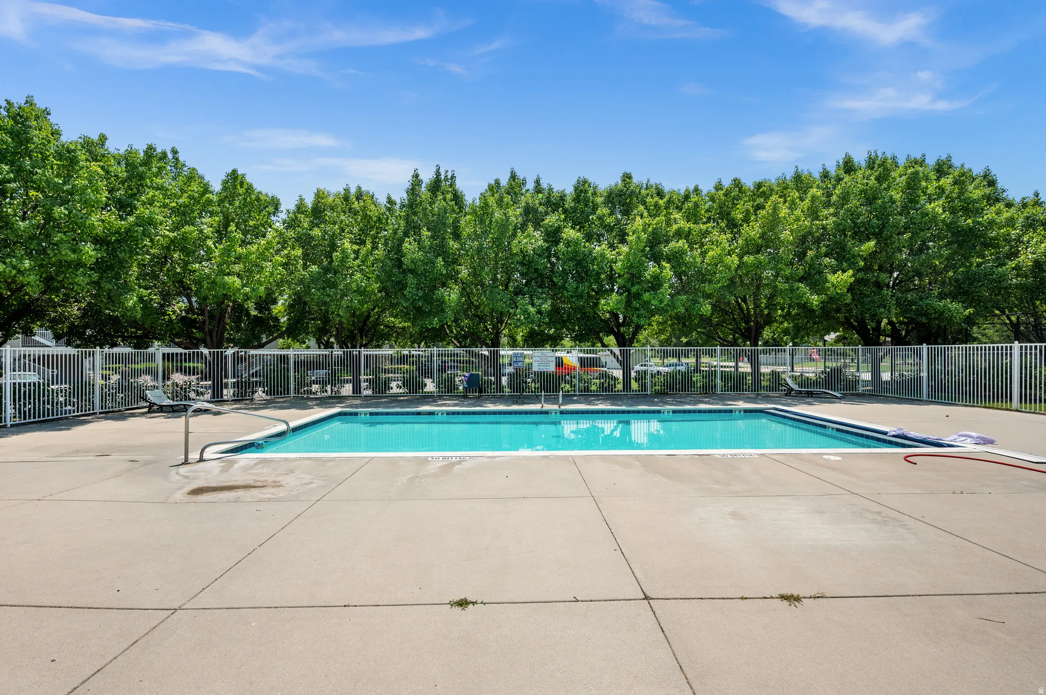 Outdoor swimming pool with integrated steps, surrounded by a concrete deck and secured by a white perimeter fence