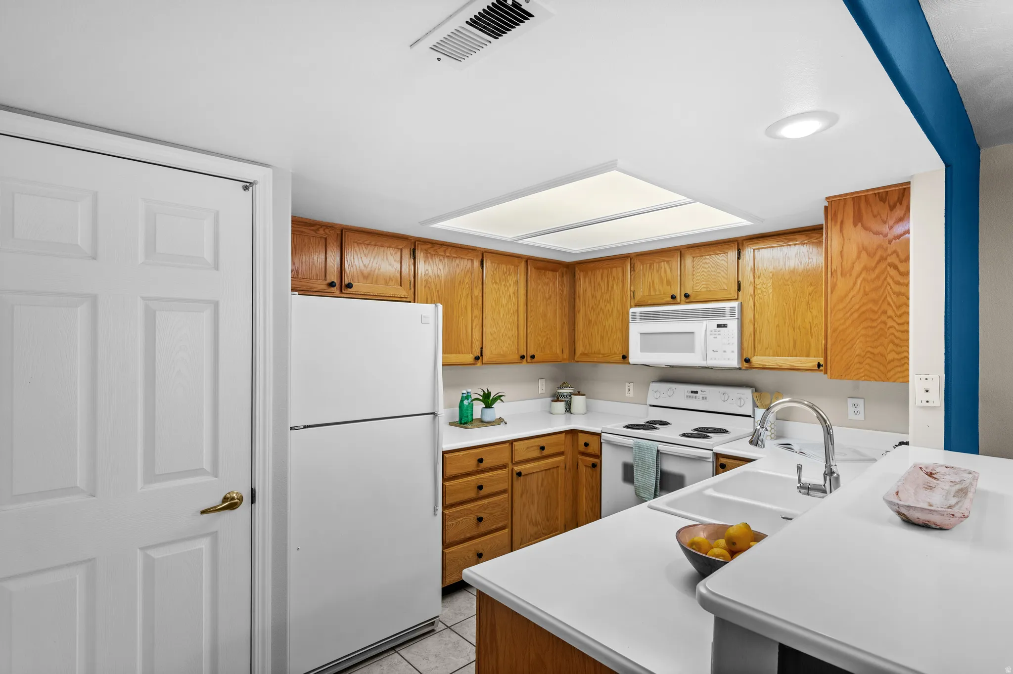 Kitchen featuring wood cabinetry, white countertops, built-in microwave, and a double basin sink