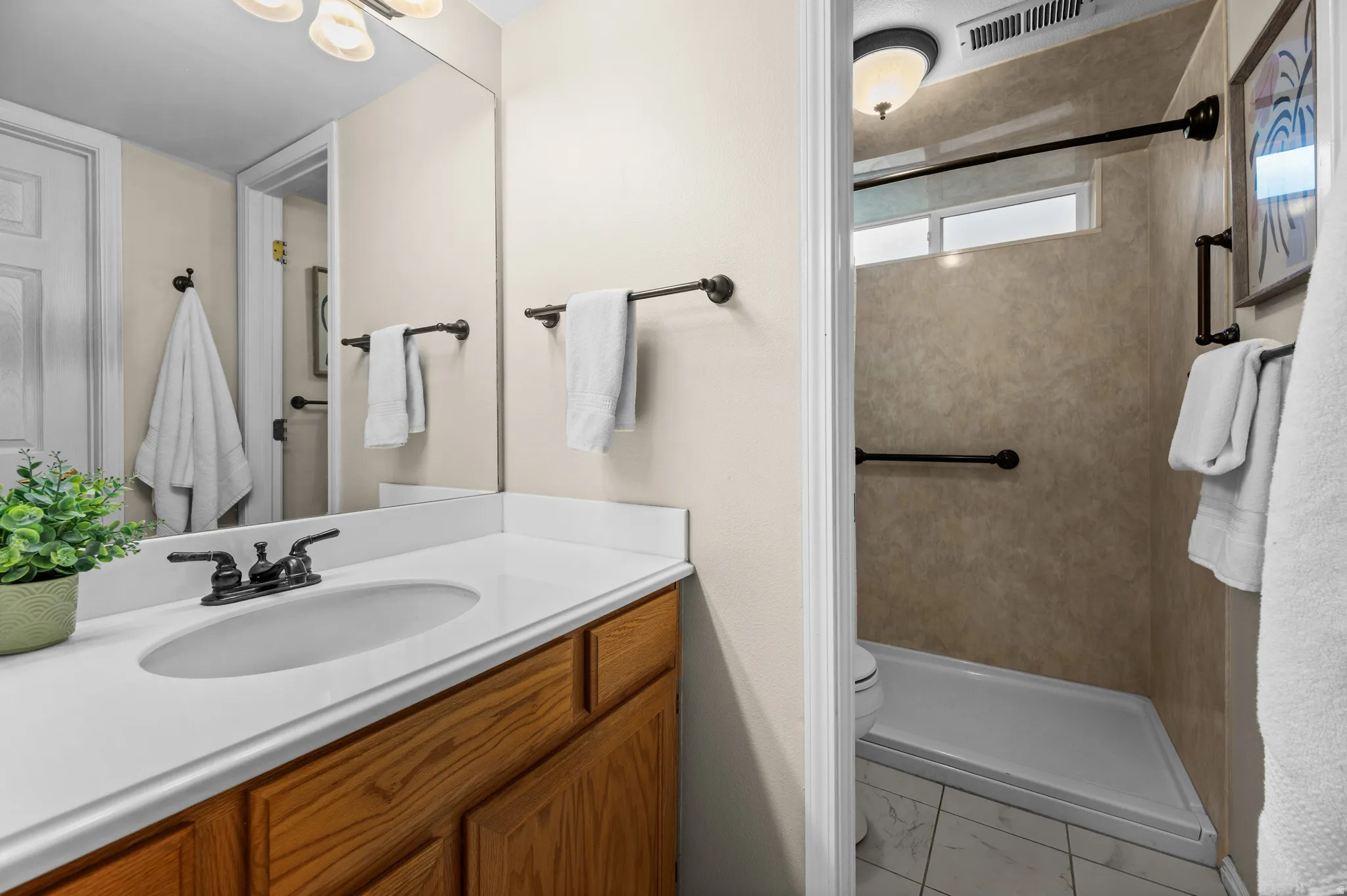 Bathroom featuring a wood-finish vanity with a white countertop and integrated sink, bronze-finish faucet, and a large wall mirror