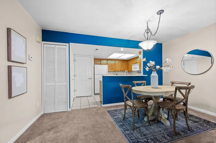 Dining area featuring a circular pendant light fixture, carpeted flooring, and a pass-through window to the kitchen