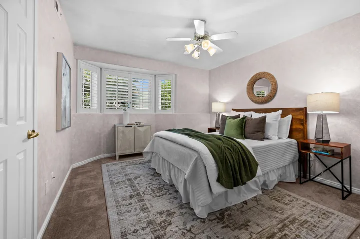 Bedroom featuring a bay window with plantation shutters, a ceiling fan with integrated lighting, and textured wall finishes