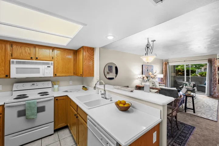 Kitchen featuring wood-finish cabinetry, white appliances, and a double basin sink with a gooseneck faucet
