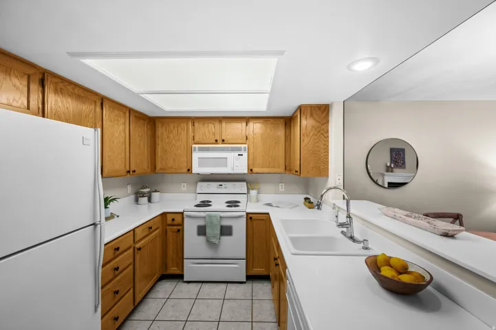 U-shaped kitchen with wood cabinetry and white appliances