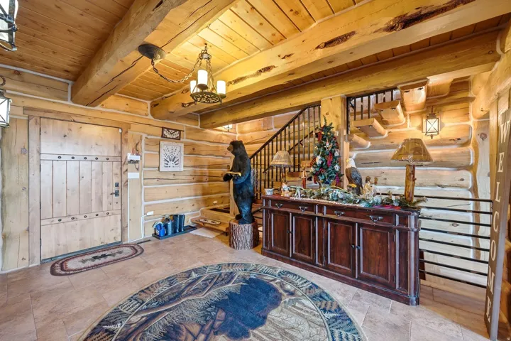 Expansive foyer featuring a solid wood entry door, natural wood-plank walls, exposed wood beams, a custom wood ceiling, and tile flooring