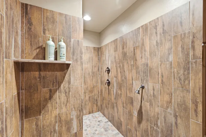 Spacious walk-in shower featuring wood-finish tile walls, dual shower heads, and a mosaic tile floor