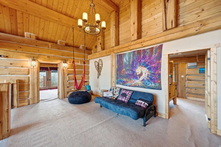Vaulted log beam ceilings featuring a central chandelier, tongue-and-groove wood paneling, and wall-mounted sconces