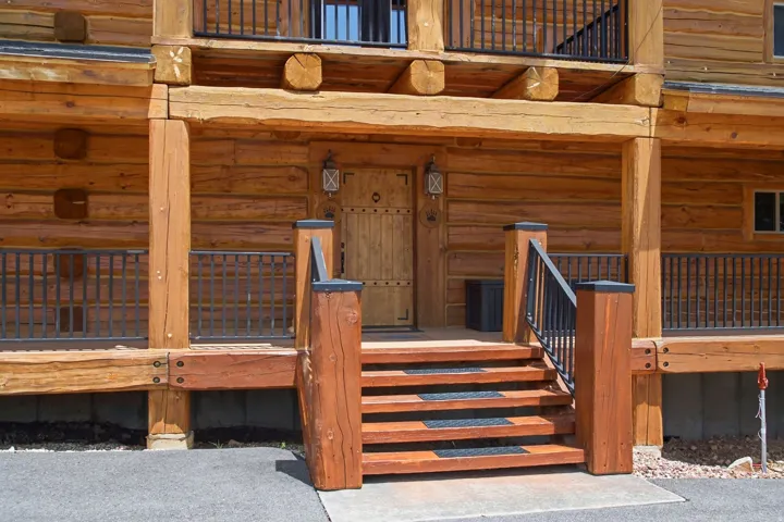 Rustic wood exterior featuring a plank-style entry door with iron hardware, a multi-tier wooden staircase, and wrought iron railings