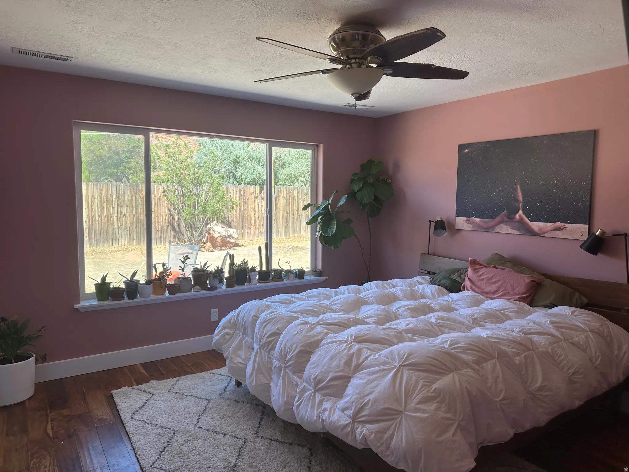 Spacious mastet bedroom featuring wood-finish flooring, a contemporary ceiling fan, and a wide window with a deep sill