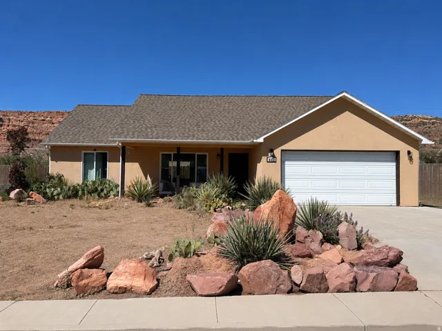Single-story stucco residence featuring a two-car garage, covered entry, and desert-inspired landscaping with natural rock elements