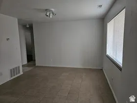 Spacious room featuring neutral-toned tile flooring, a large window with blinds, and white walls