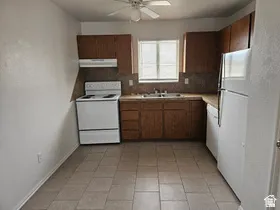 Kitchen with tile flooring, wood cabinetry, built-in sink, and white appliances