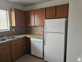 Kitchen area featuring wood-finish cabinetry, a double basin stainless steel sink, and a white refrigerator