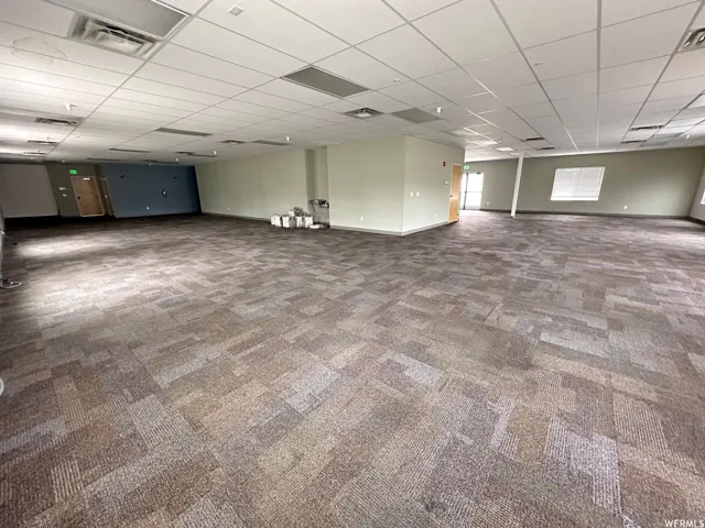 Spacious open-concept commercial interior featuring patterned carpet tiles, drop ceiling with integrated lighting, multiple entryways, and ample wall space