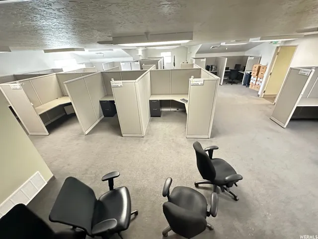 Open-concept office space featuring multiple workstations, neutral-toned carpeting, and white walls