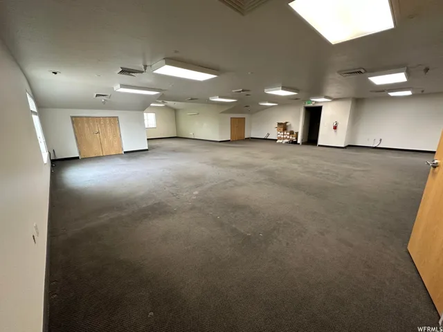 Spacious room featuring broadloom carpeting, multiple recessed lighting fixtures, and light wood-finish doors