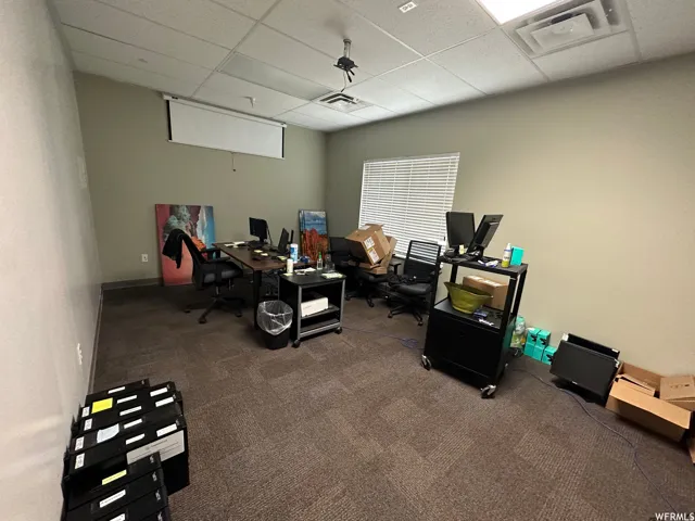 Spacious commercial room featuring neutral-toned walls, a drop ceiling with recessed lighting, and a window with horizontal blinds