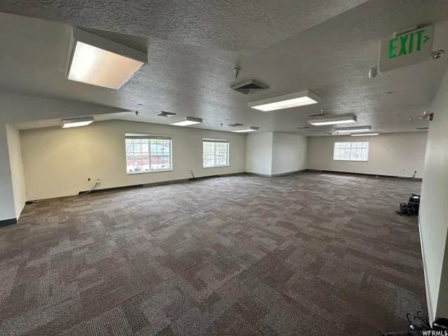 Spacious room featuring multiple windows, neutral wall tones, patterned carpet flooring, and integrated ceiling lighting