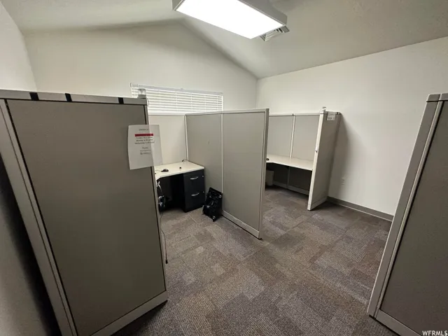 Office workspace featuring modular cubicles, neutral carpeting, vaulted ceilings, and fluorescent lighting