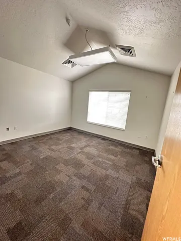 Interior room featuring a gabled ceiling and a large window with horizontal blinds