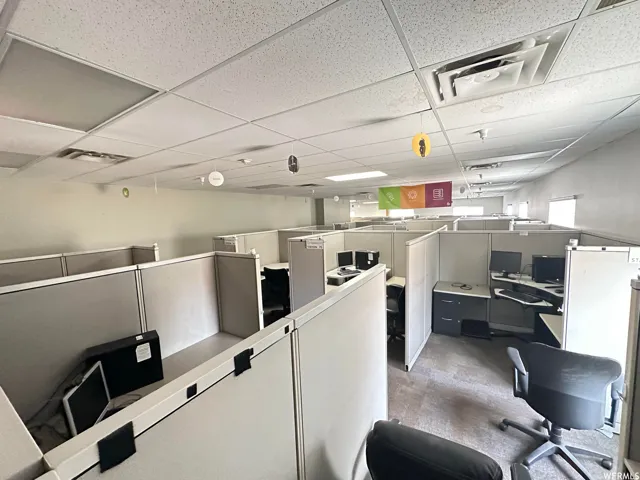 Open office space featuring multiple workstations, modular cubicle walls, recessed lighting, drop ceiling, and carpeted flooring