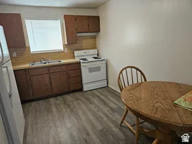 Kitchen featuring dark wood-finish cabinetry, a white electric range, a double basin stainless steel sink, and wood-finish flooring
