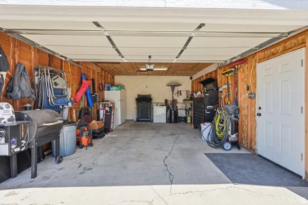 Spacious garage with concrete flooring, exposed wood-paneled walls, and a white access door