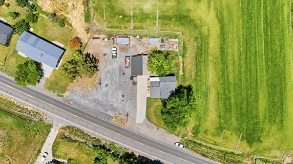 Expansive property featuring a paved driveway, a large gravel parking area, mature trees, and a substantial green field