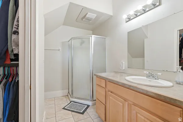 Bathroom featuring a corner glass shower enclosure, single vanity with a laminate countertop, undermount sink, and tiled flooring