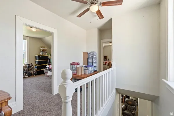 Carpeted upper landing featuring white painted balusters and a wood-finish ceiling fan with integrated lighting