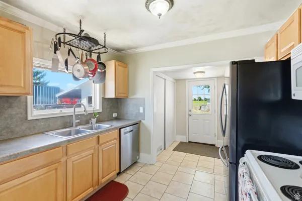 Kitchen featuring light wood cabinetry, a double basin stainless steel sink, a stainless steel dishwasher, a black refrigerator, and tile flooring