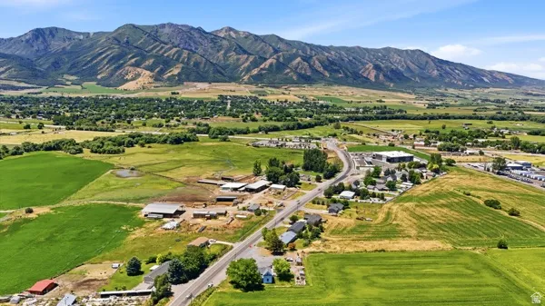 Expansive aerial showcasing a mountainous backdrop, extensive green fields, and scattered residential and commercial structures