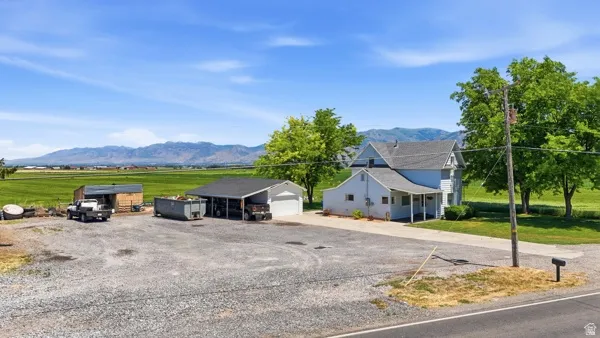 Expansive gravel lot featuring a two-story residence with a covered porch and a detached garage with an attached carport
