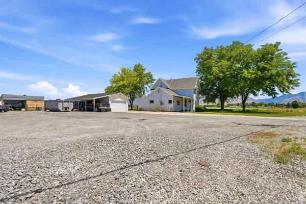 Expansive gravel area providing ample open-air parking, alongside a white residence with covered porch, detached garage, and additional covered structures
