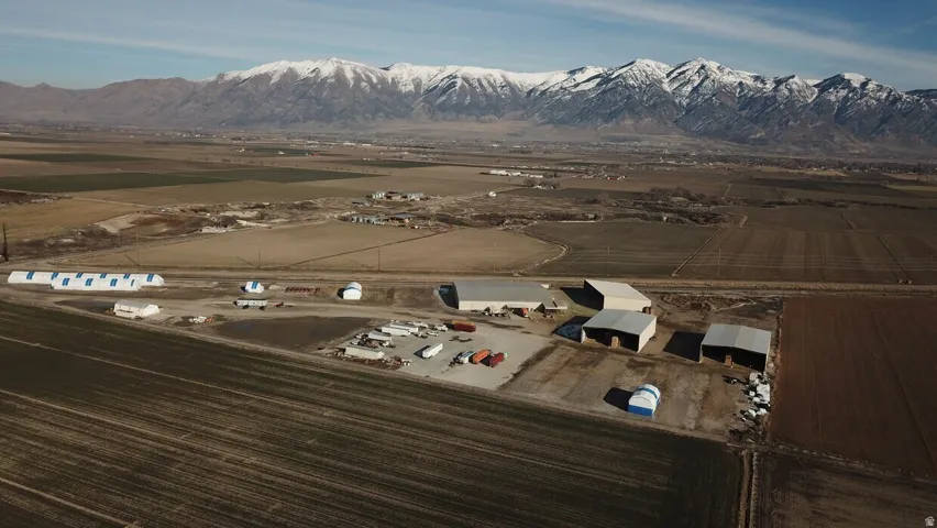 Agricultural property featuring multiple outbuildings, expansive fields, and a distant mountain range with snow-capped peaks
