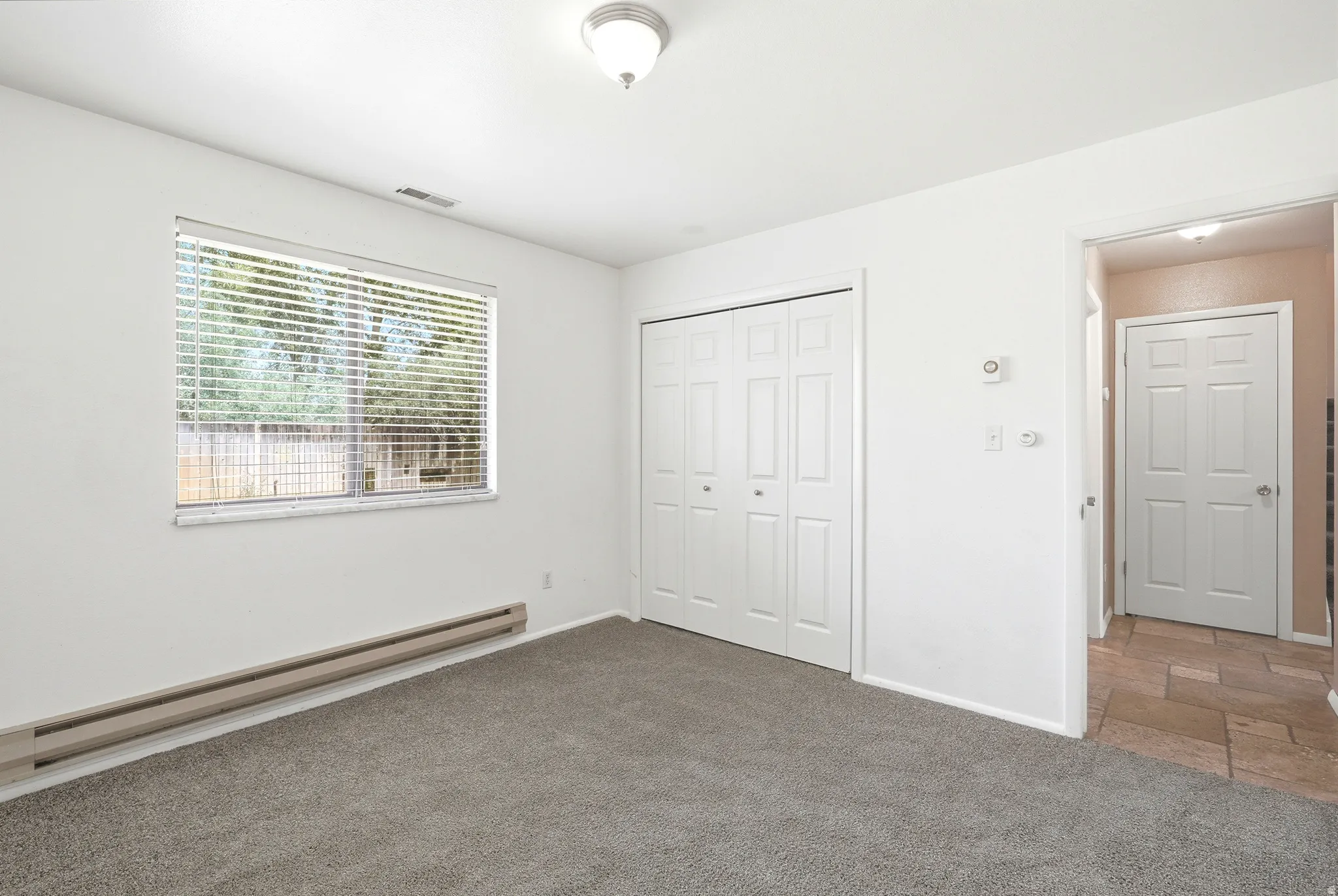 Carpeted room with a large window, bi-fold closet doors, and baseboard heating