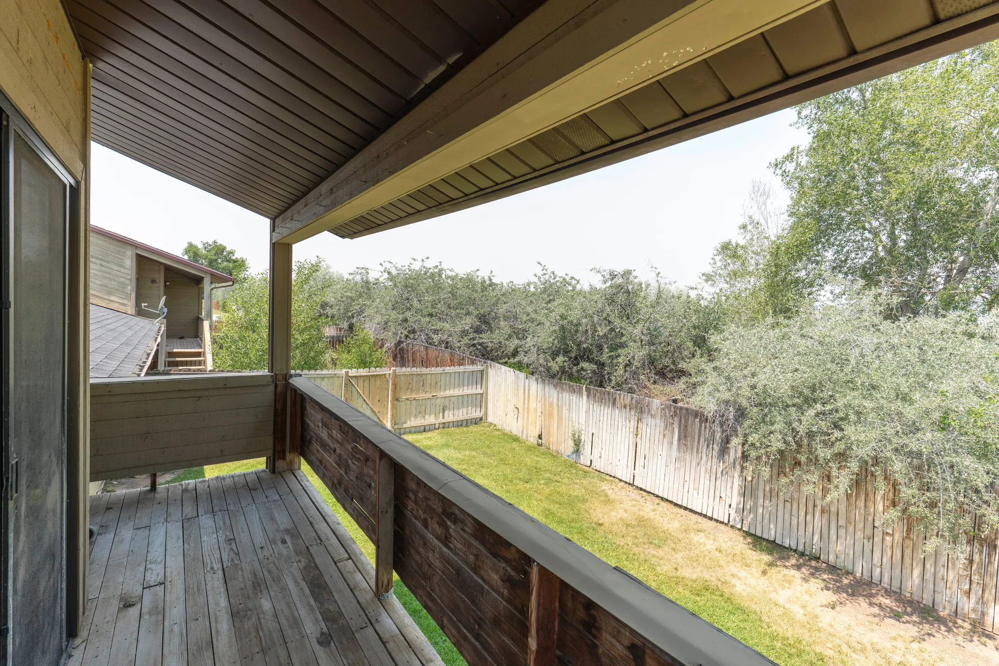Private balcony featuring wood-finish decking and a wooden privacy fence enclosing a grassy yard