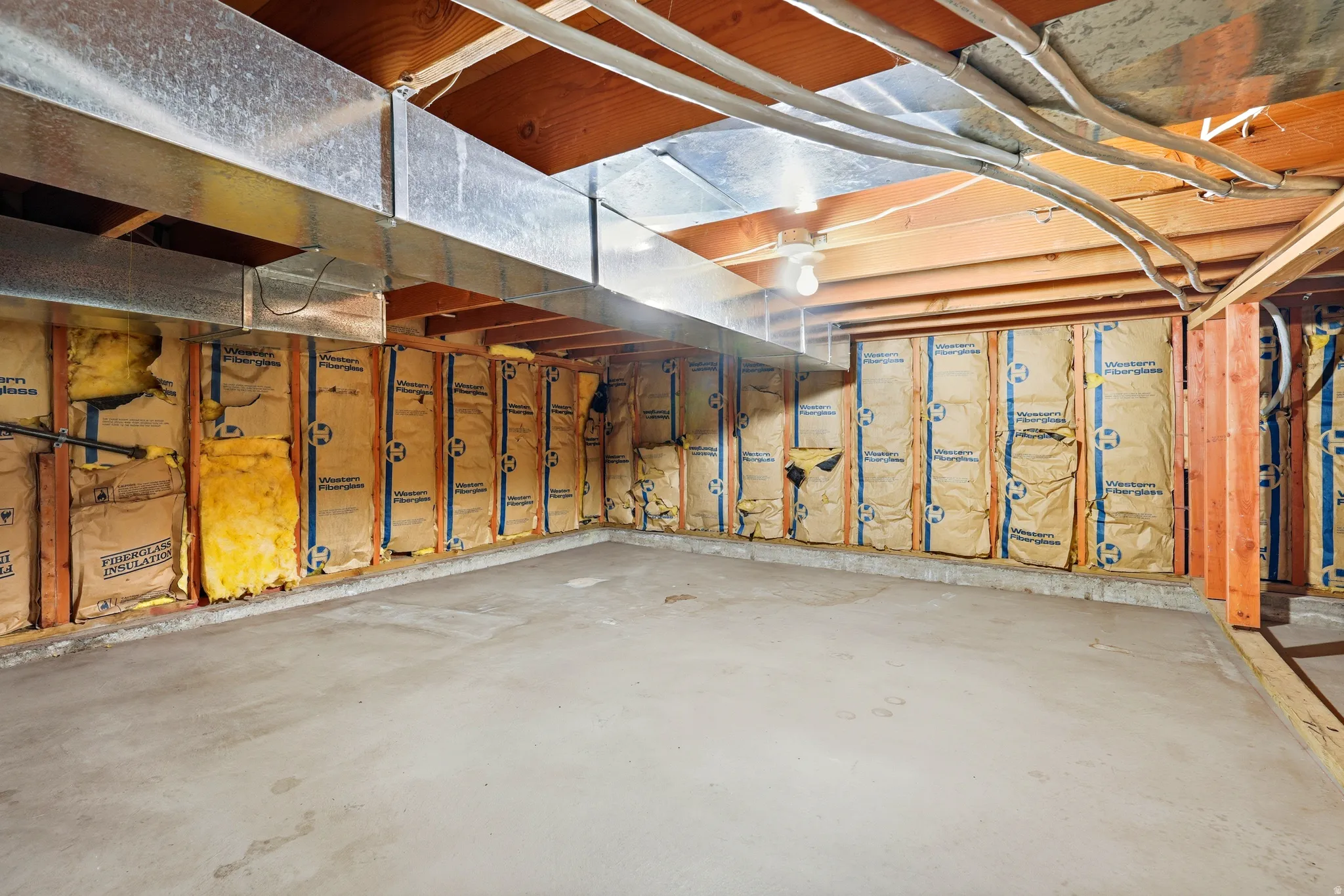 Unfinished crawl space featuring exposed wooden ceiling joists, galvanized ductwork, and insulated wall framing