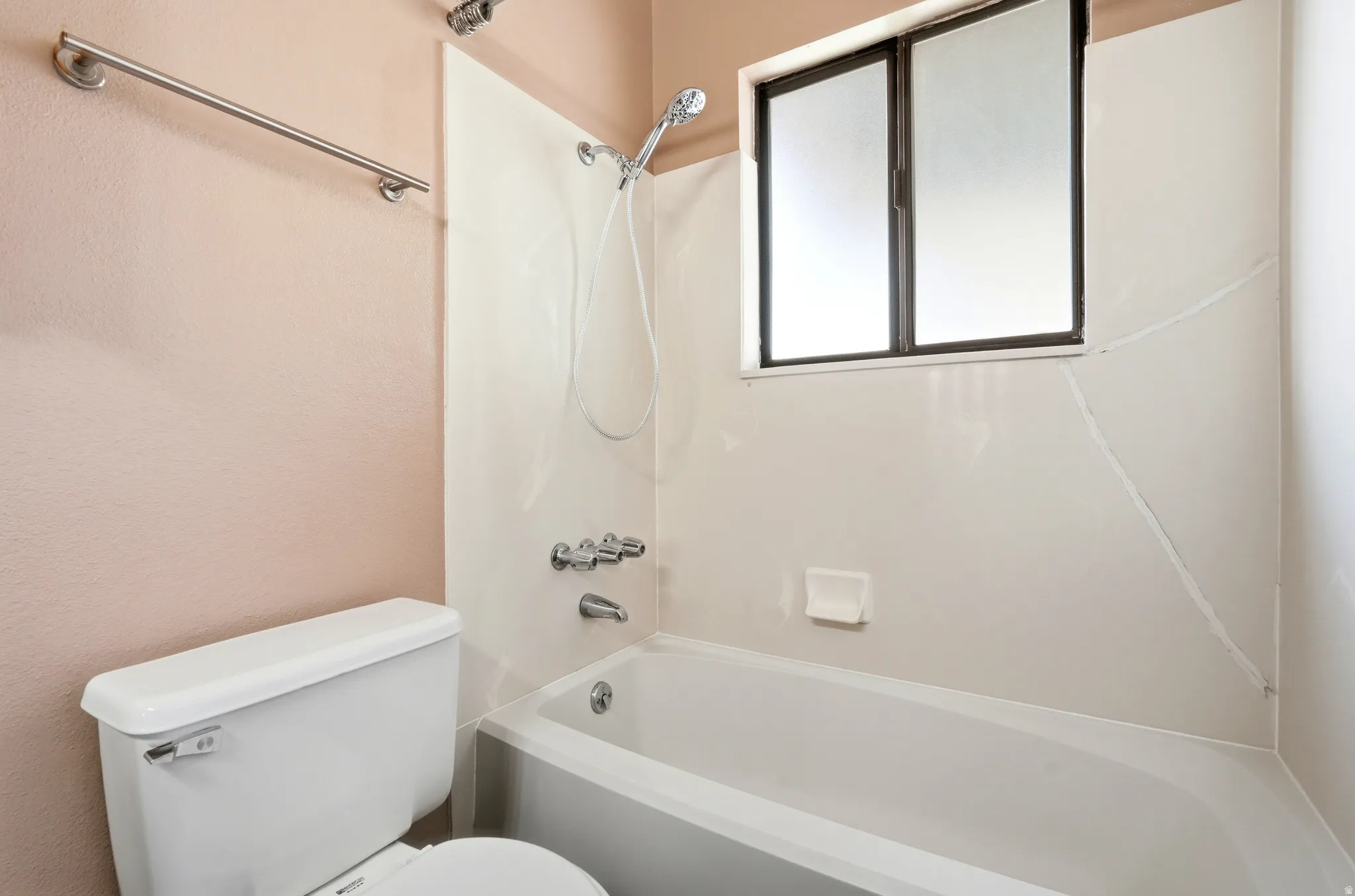 Bathroom featuring a white tub-shower combination with a showerhead and separate faucet, a window with frosted panes, and a white toilet