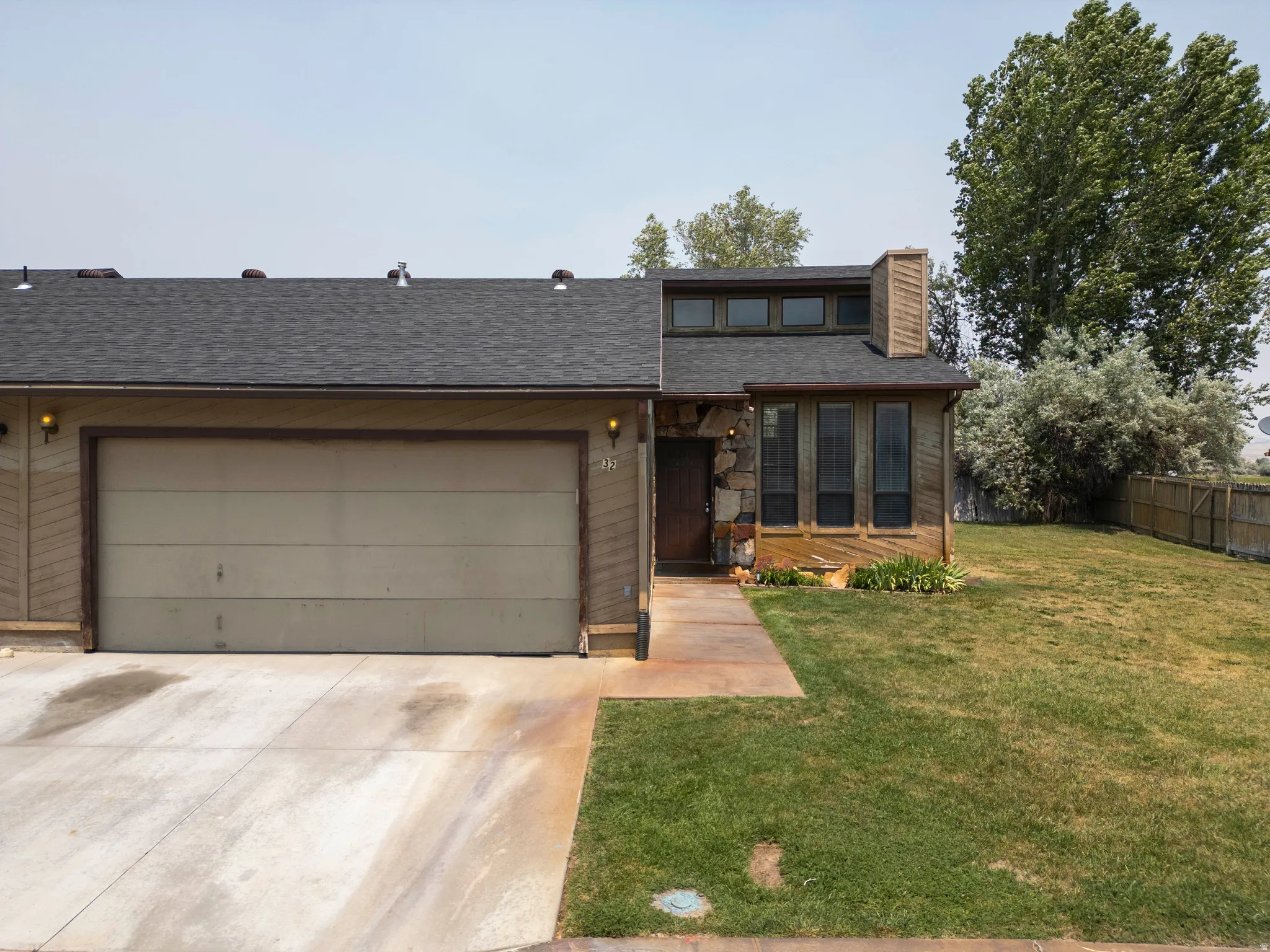 Residence featuring a two-car garage, stone and wood-paneled facade, and a dark asphalt shingle roof