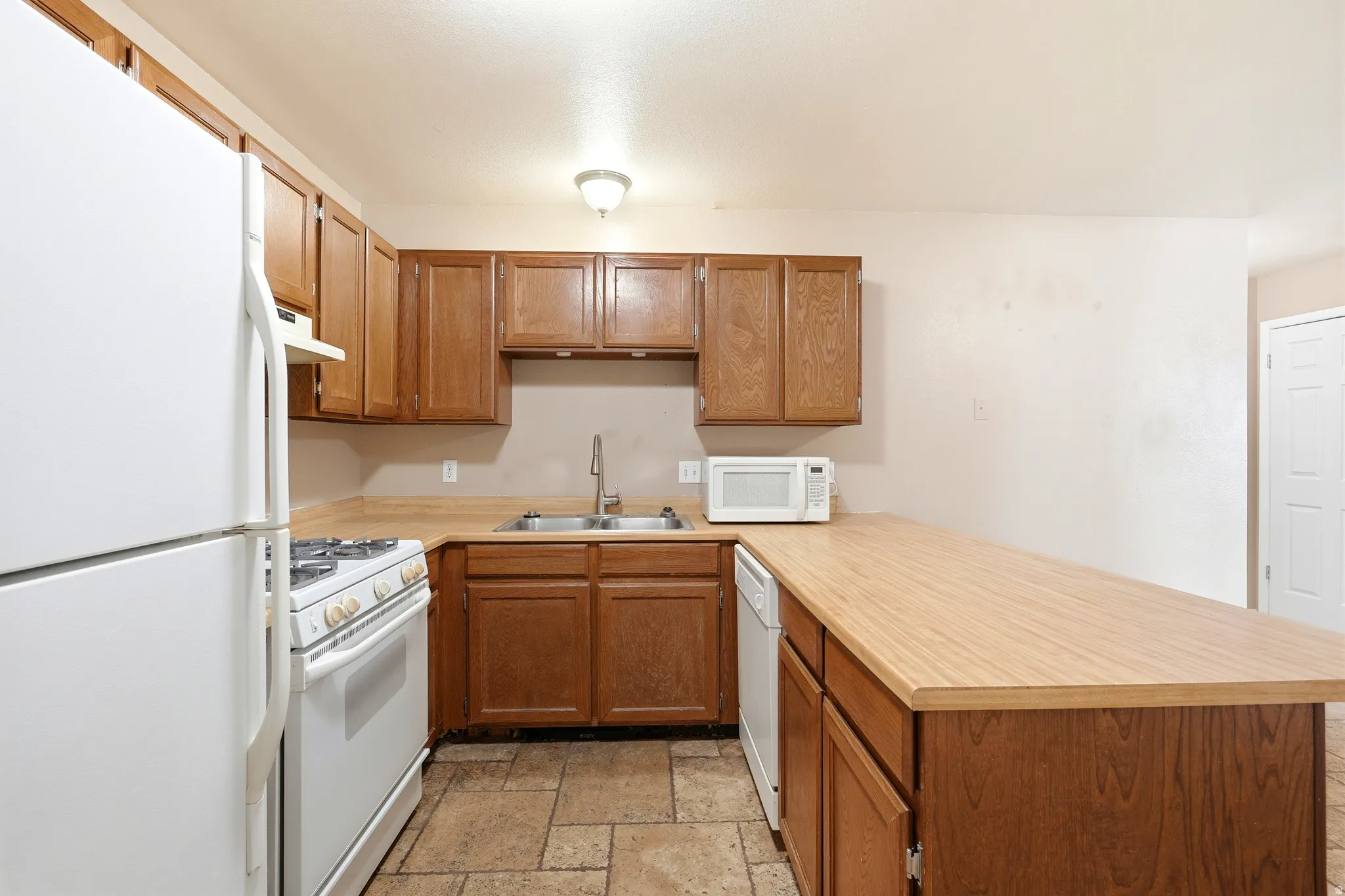 Kitchen featuring wood cabinetry, stainless steel sink, tile flooring, wood-finish countertops, and white appliances