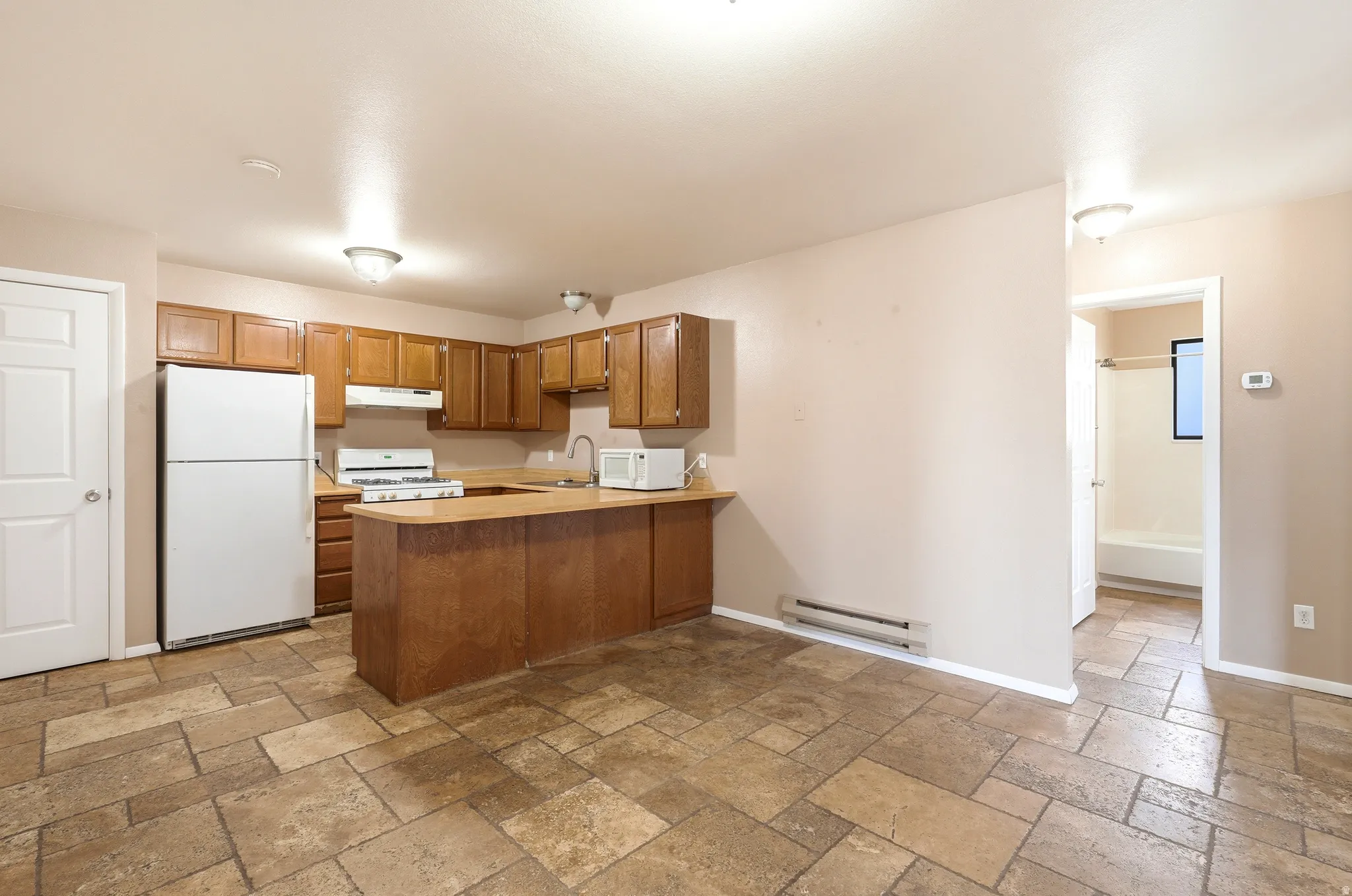 Kitchen featuring wood cabinetry, white appliances, and a peninsula countertop