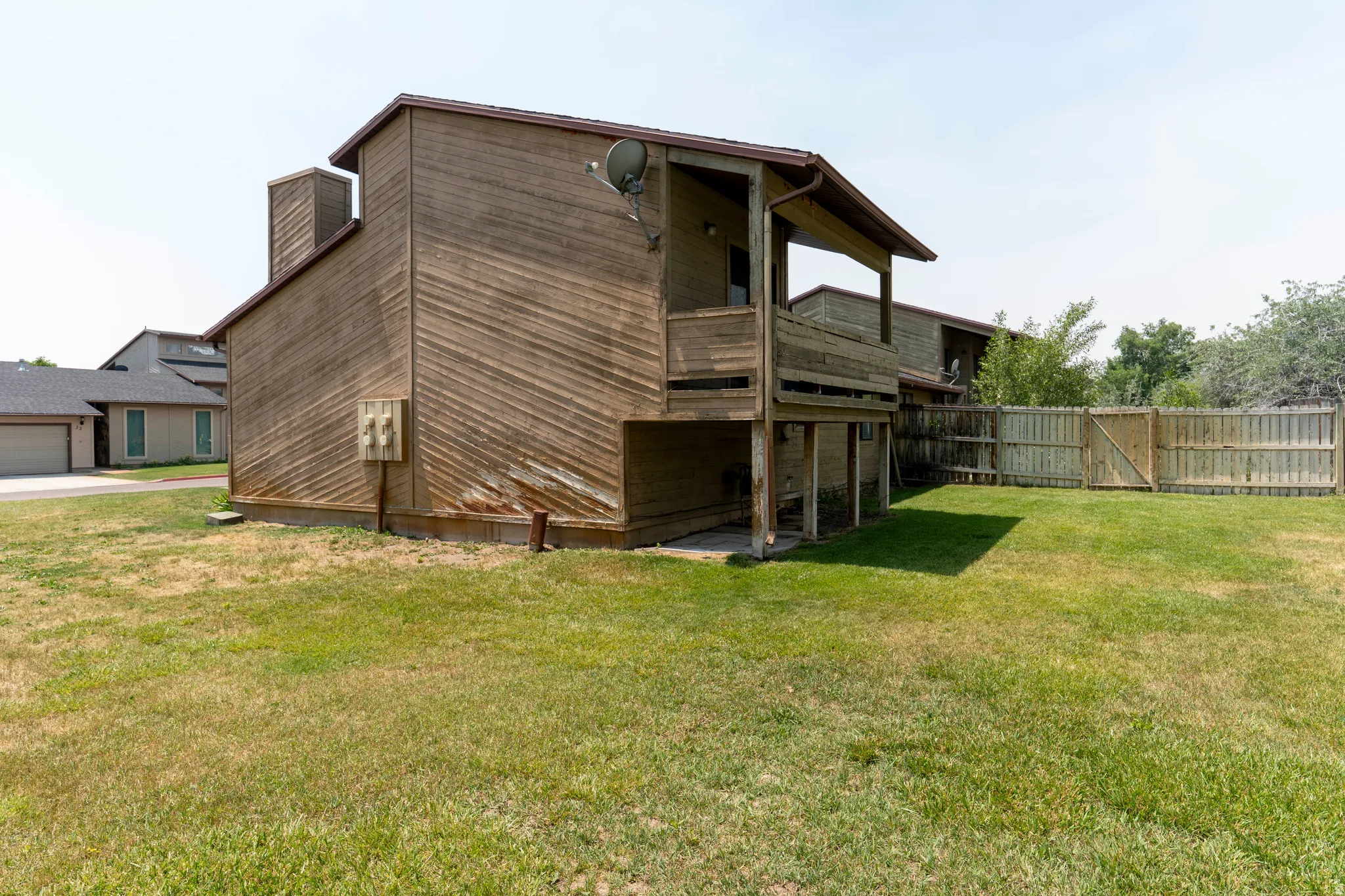 Wood-sided exterior featuring an upper-level balcony, ground-floor patio, and a wood fence enclosing a grassy yard
