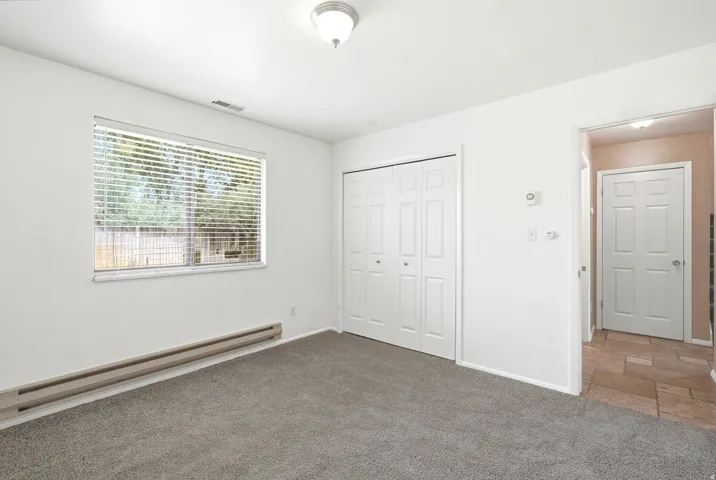 Carpeted room with a large window, bi-fold closet doors, and baseboard heating