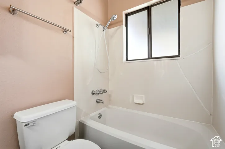Bathroom featuring a white tub-shower combination with a showerhead and separate faucet, a window with frosted panes, and a white toilet